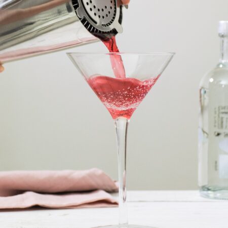 Red cosmopolitant being poured from a shaker in a martini glass