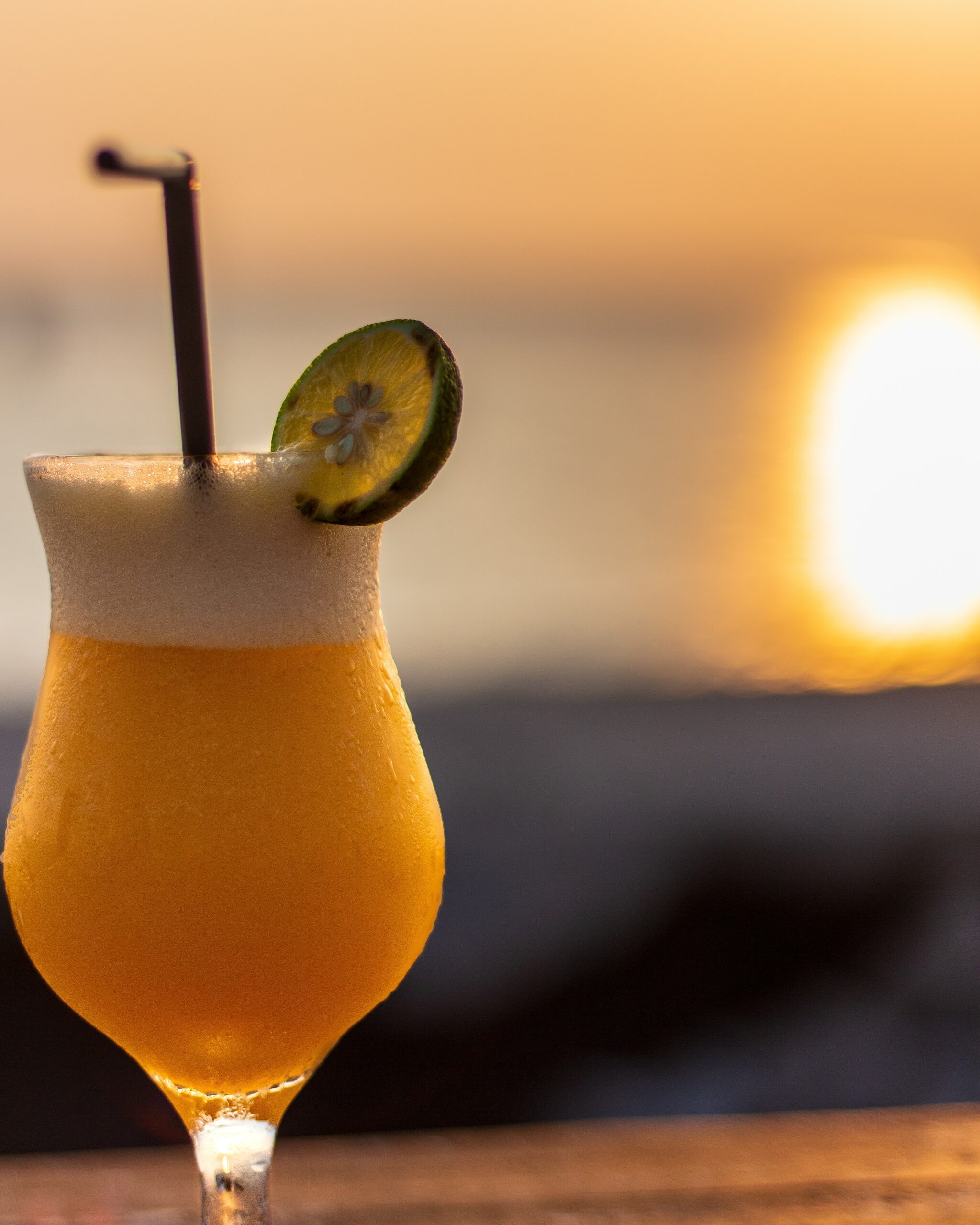 Mango cocktail with straw and lemon slice pictured at sunset