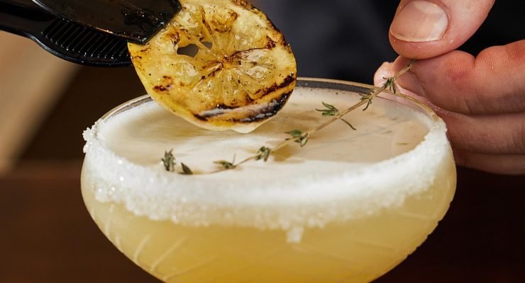 Bee’s Knees cocktail in coupeglas met suikerrand, gegarneerd met gegrilde citroen en tijm – klassieke roaring twenties cocktail.